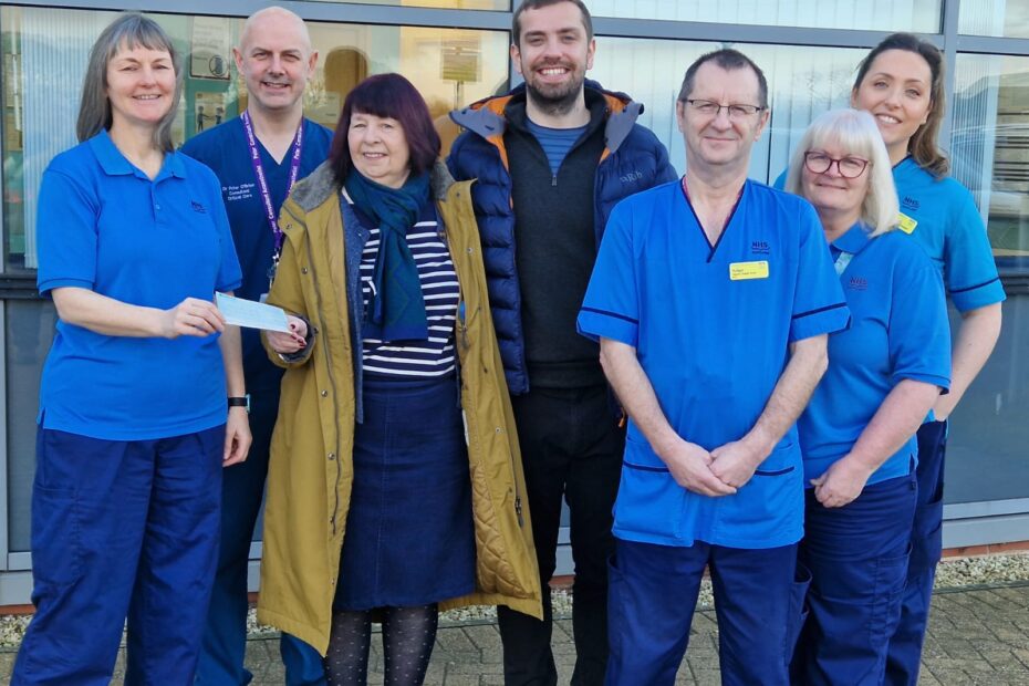 Staff standing in front of hospital building receiving the donation cheque from Keir Williams